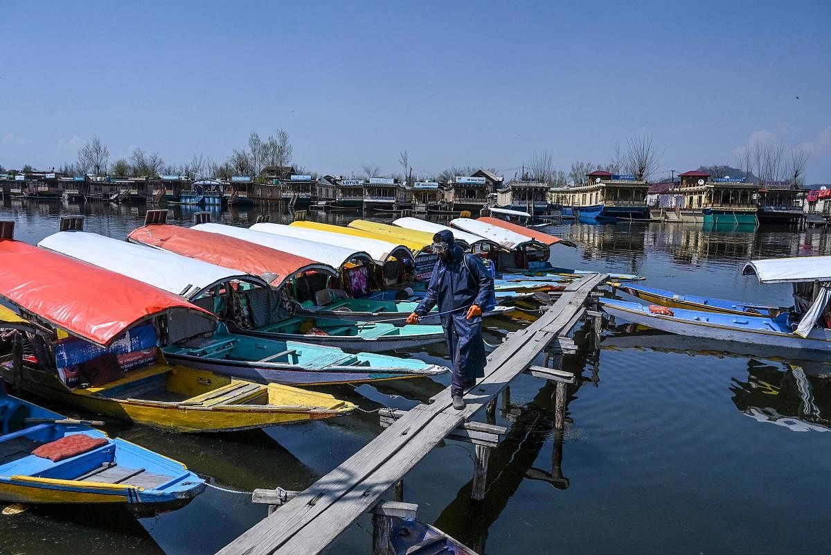A municipal worker sprays disinfectant on boats amid concerns over the spread of the COVID-19 novel coronavirus at Dal lake in Srinagar. (PTI Photo)