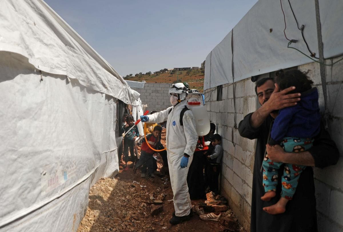 A member of the Syrian Civil Defence, also known as the "White Helmets", disinfects a tent in the Kafr Lusin camp for the displaced by the border with Turkey, in Syria's rebel-held northwestern province of Idlib, on March 24, 2020, as part of efforts to prevent the spread of coronavirus. Credit: AFP Photo