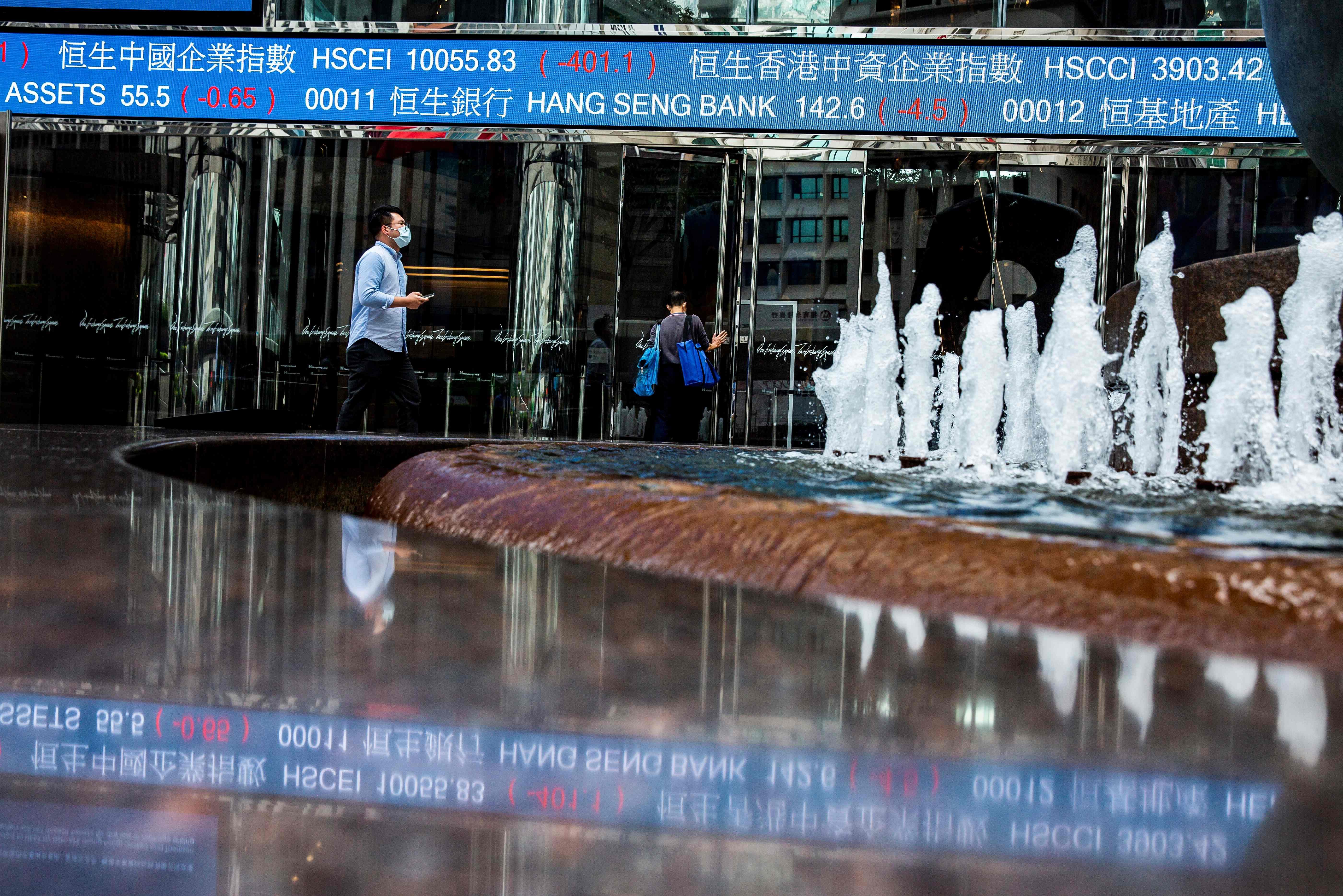 An electronic ticker board displays various stock prices as a mask-clad pedestrian walks past at Exchange Square in Hong Kong. (Credit: AFP)