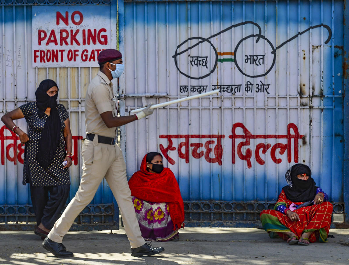 Policeman stands guard outside a government school as people gather to receive free meals distributed by volunteers during the nationwide lockdown, in New Delhi, Friday, March 27, 2020. (PTI Photo)