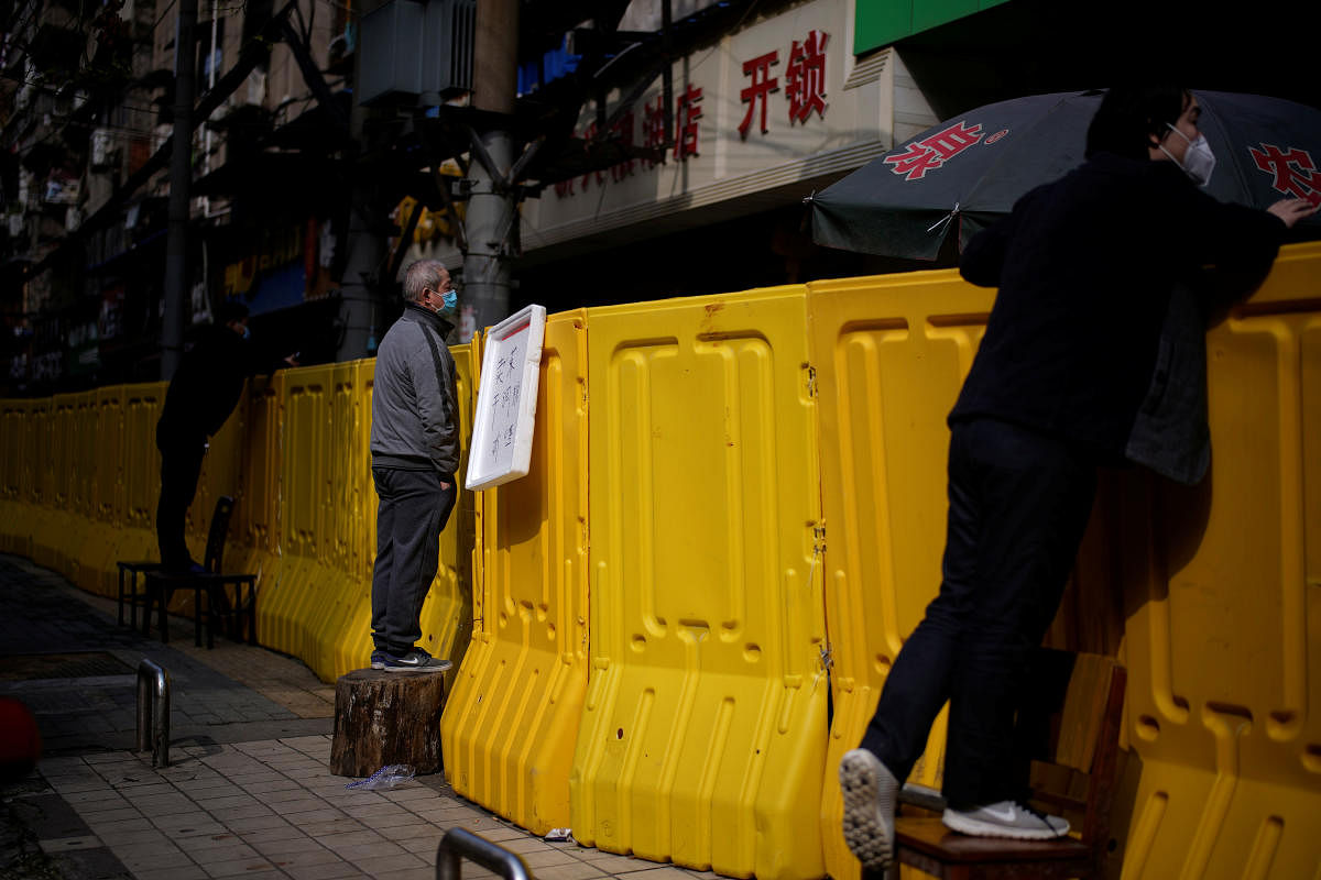Residents wearing face masks pay for groceries by standing on chairs to peer over barriers set up to ring fence a wet market on a street in Wuhan. Credit: Reuters Photo