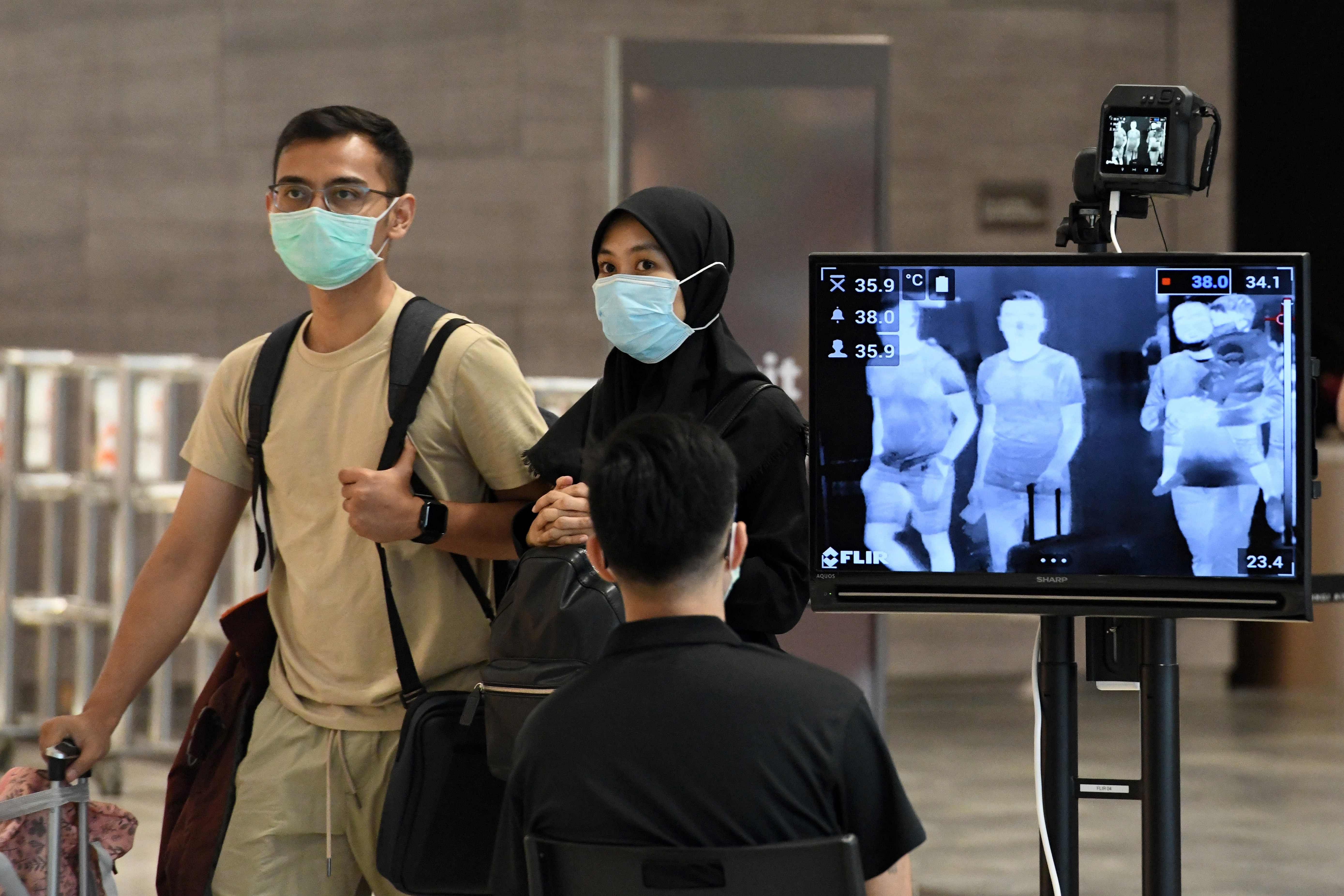 A couple, wearing facemasks amid fears about the spread of the COVID-19 novel coronavirus, walk past a temperature screening check at Changi International Airport. (AFP Photo)