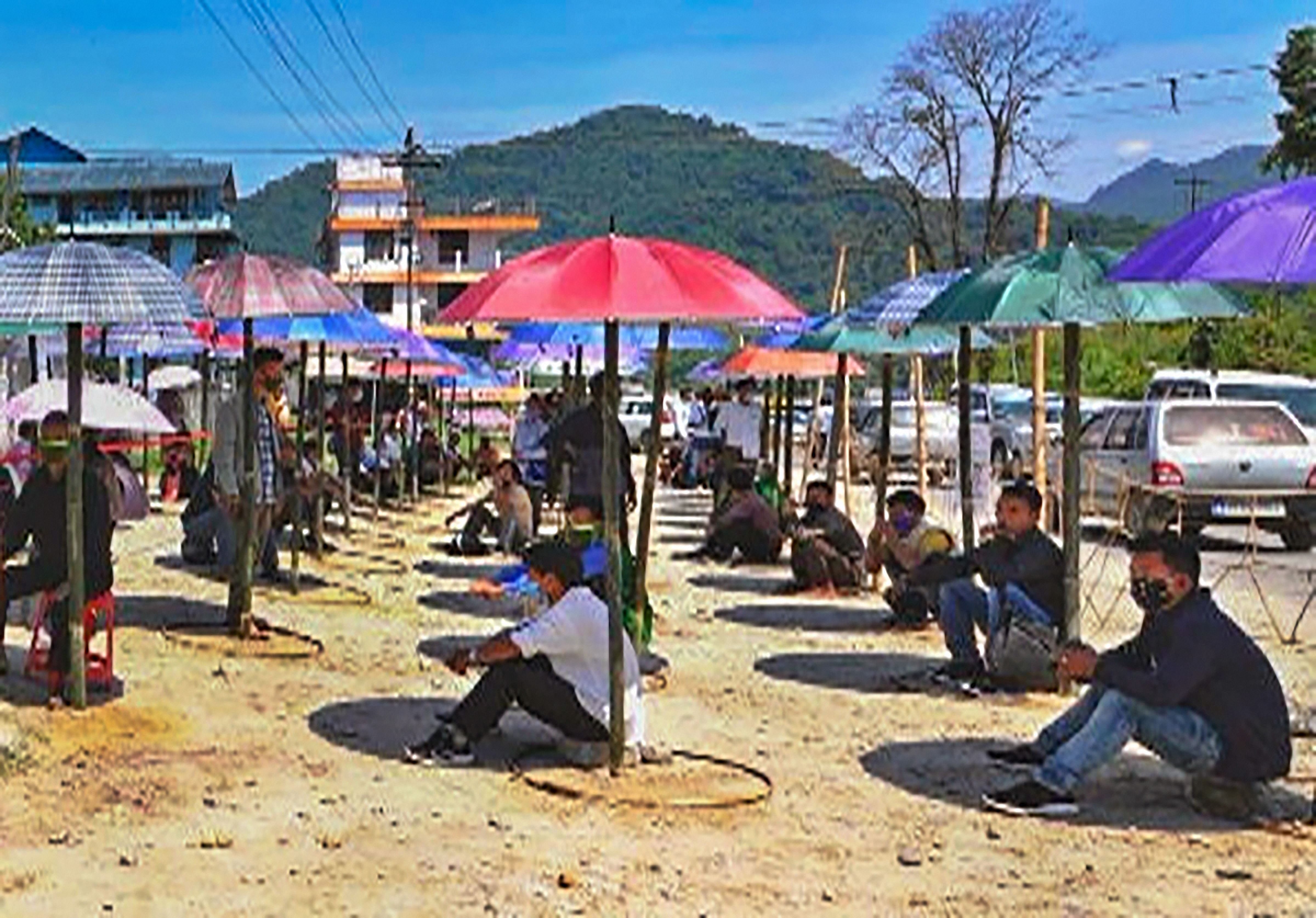 Locals wait under a shed made of garden umbrellas in front of a bank, during the ongoing COVID-19 nationwide lockdown, in West Siang district. (Credit: PTI Photo)
