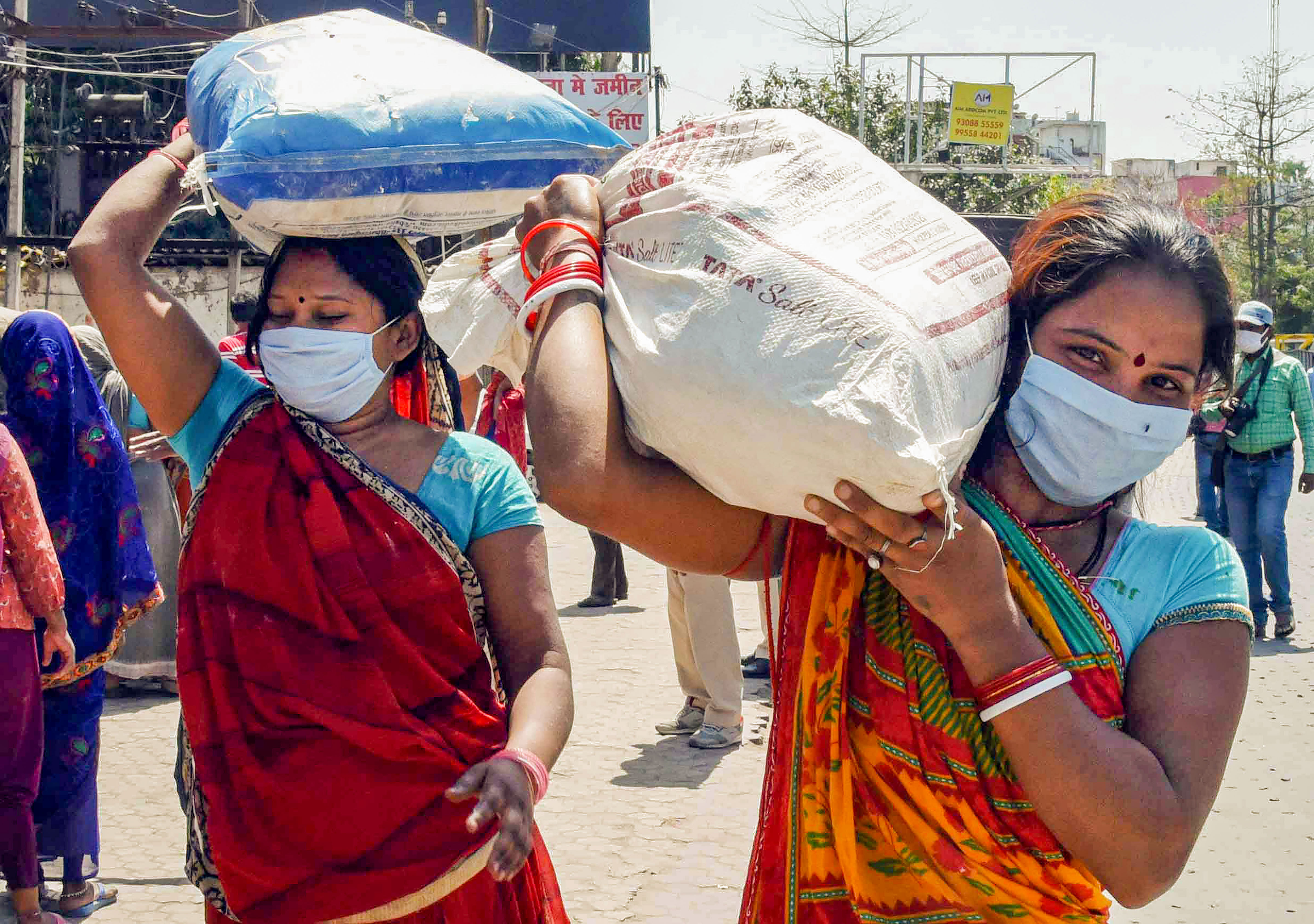 Patna: Needy people wearing protective masks carry relief material given by the security personnel during the nationwide lockdown imposed in the wake of coronavirus pandemic. (Credit: PTI)