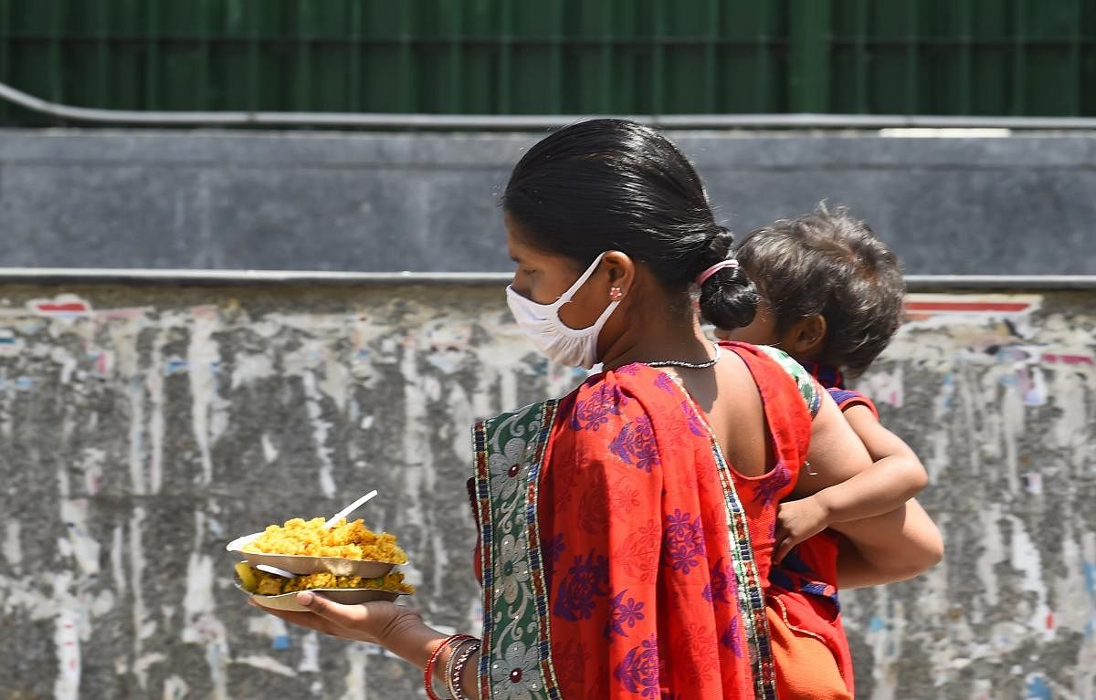 A woman, carrying a child, walks back after collecting food from volunteers near the AIIMS, during the nationwide complete lockdown (PTI Photo)