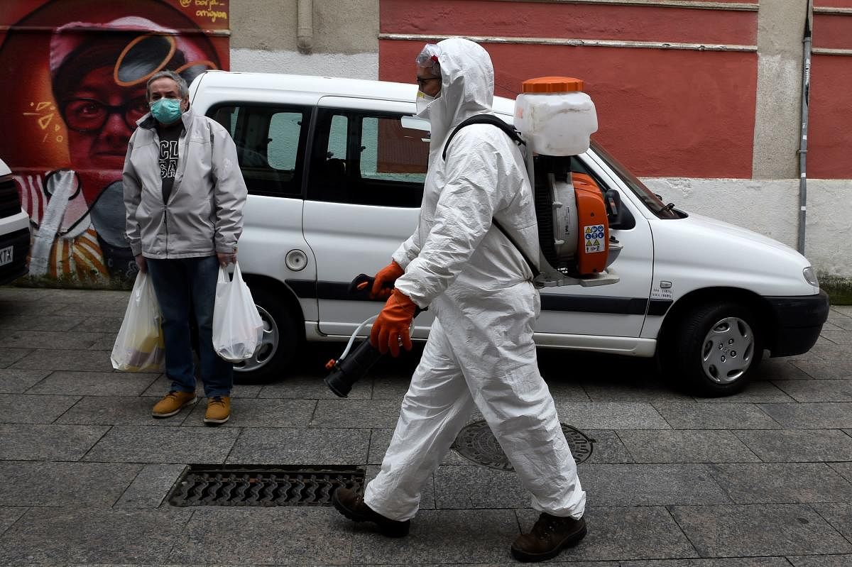 A man dressed in protective gear carries out disinfection works in a street of Spain (AFP Photo)