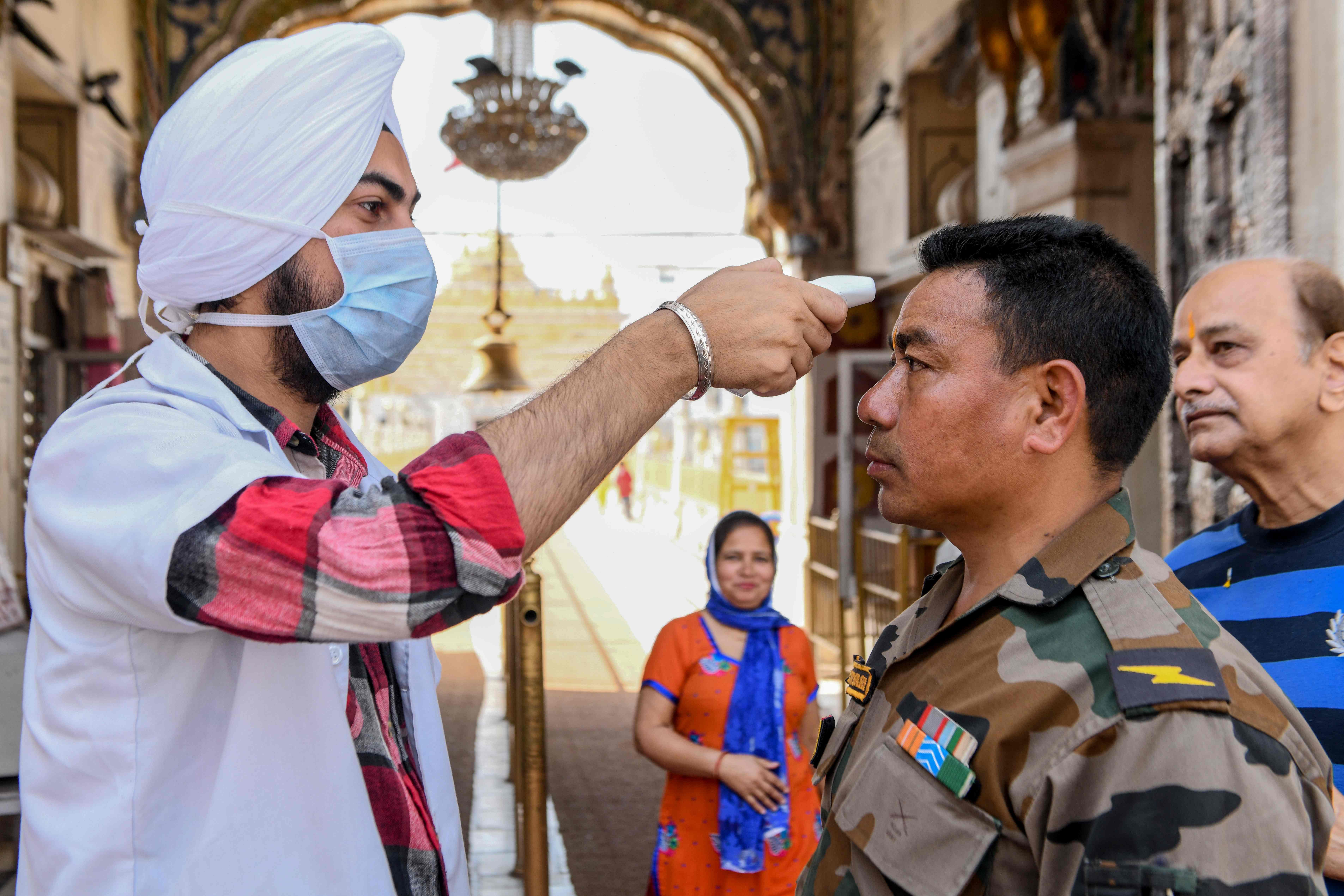 A health worker (L) wearing a facemask checks the body temperature of an army personnel, amid concerns over the spread of the COVID-19 novel coronavirus, at the entrance of the Durgiana Temple in Amritsar. (Credit: AFP Photo)