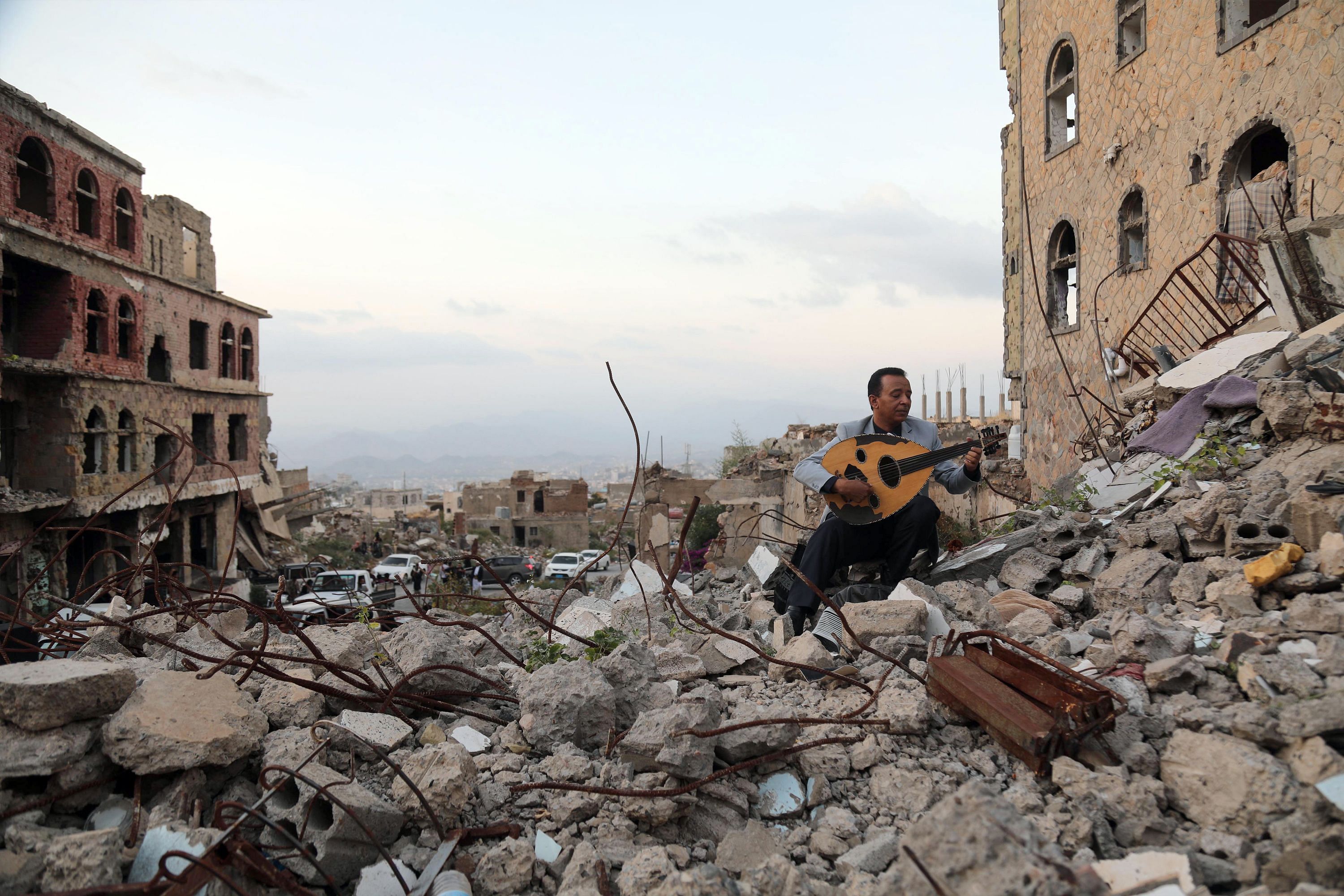In this file photo taken on December 06, 2019 a Yemeni artist sits atop the rubble of a collapsed building, as he plays the Oud. (Credit: AFP Photo)