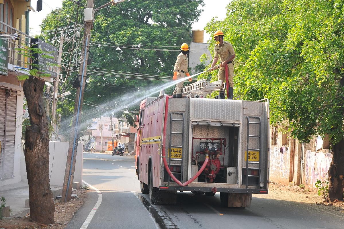 Fire and Emergency Services personnel spray disinfectant at MJ Nagar in Hosapete, Ballari district, on Friday. DH Photo