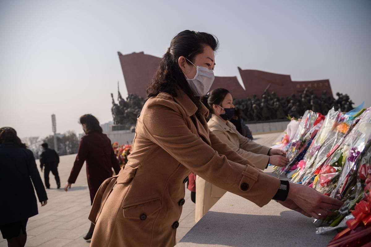 People wearing face masks lay flowers before the statues of late North Korean leaders Kim Il Sung and Kim Jong Il on the occasion of the 108th birthday of late North Korean leader Kim Il Sung. AFP