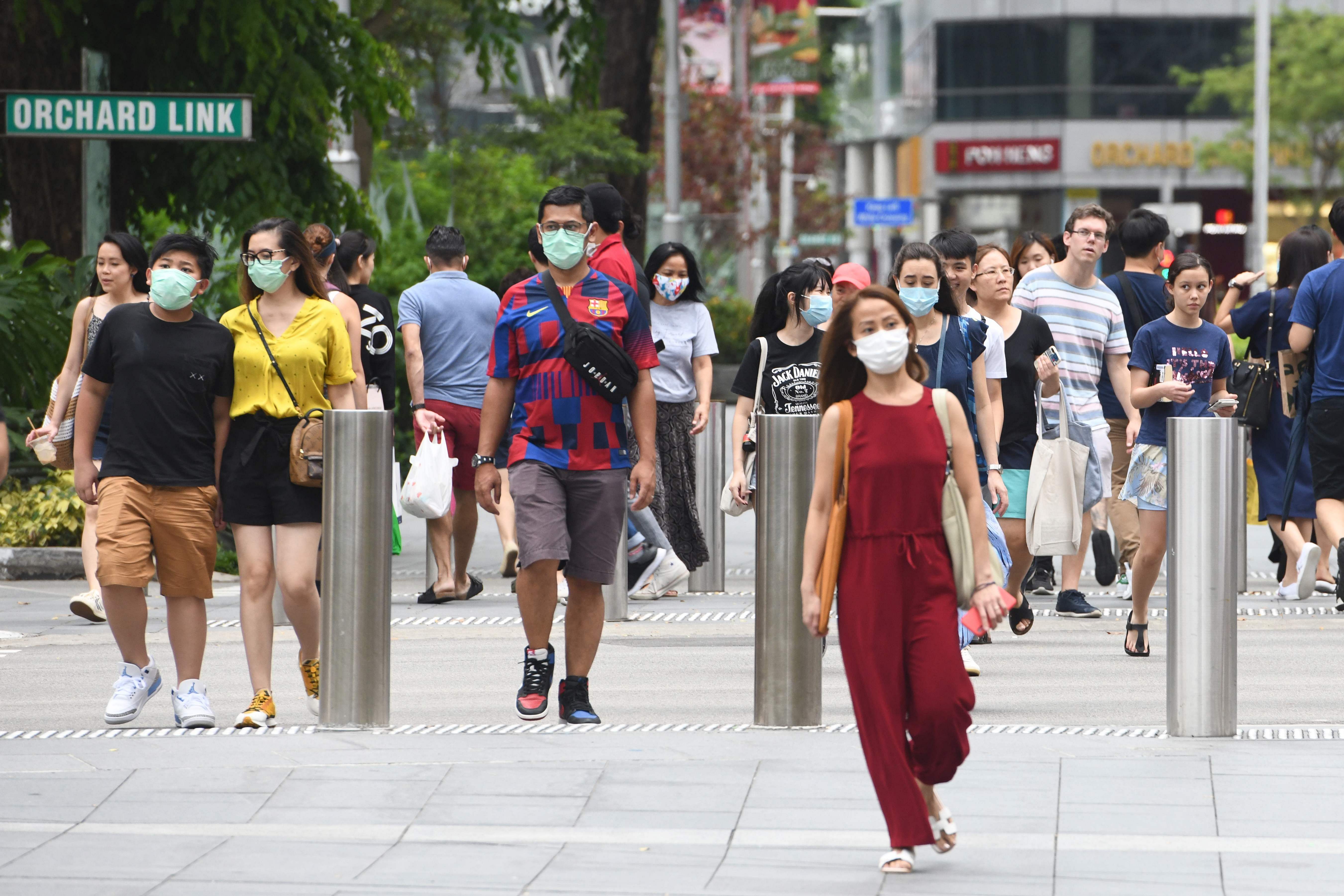 People wear facemasks to try to halt the spread of the COVID-19 coronavirus as they walk through a shopping district on Orchard Road in Singapore. (Credit: AFP Photo)