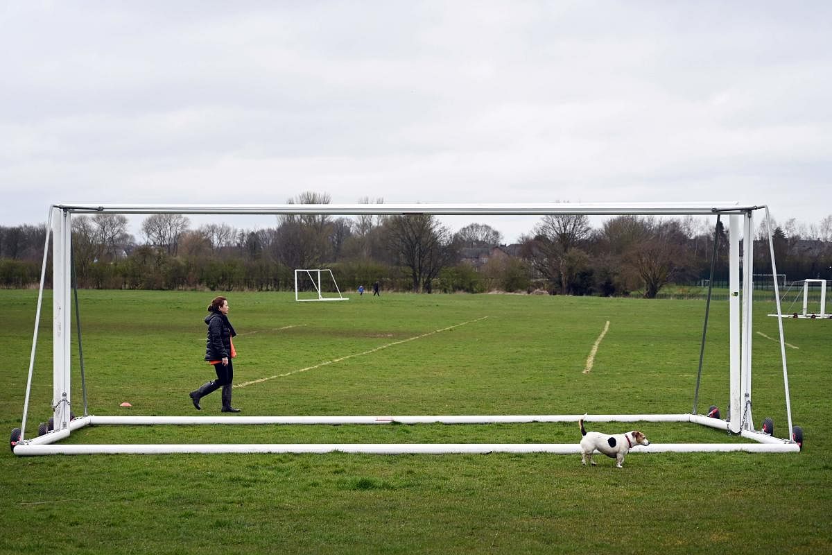 A woman walks her dog past locked football goals (AFP Photo)