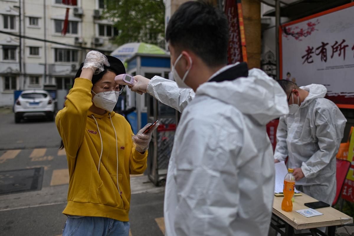 A man wearing a protective suit checks a woman's temperature next to a residential area in Wuhan, in China (AFP Photo)