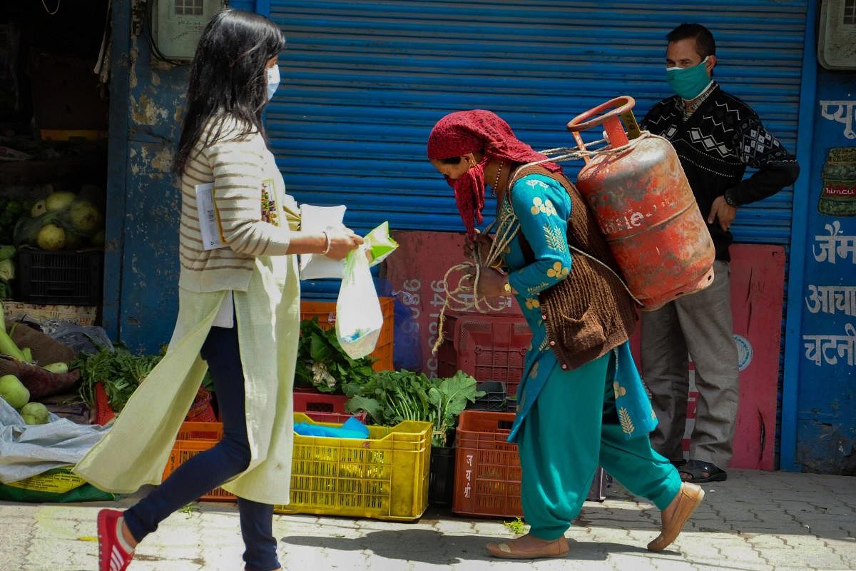 A woman carries a LPG cylinder on her back as another woman walks past her, during the nationwide lockdown to curb the spread of coronavirus, in Kullu, Monday, April 27, 2020. (PTI Photo)
