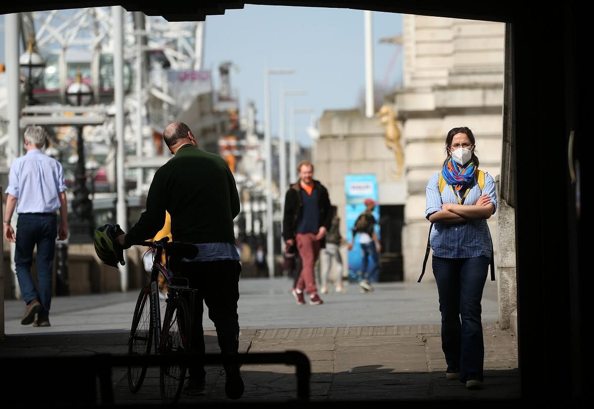 A woman wearing a face mask as a precautionary measure against COVID-19, walks past a cyclist on the South Bank, by the River Thames in central London on April 7, 2020. Credit: AFP Photo