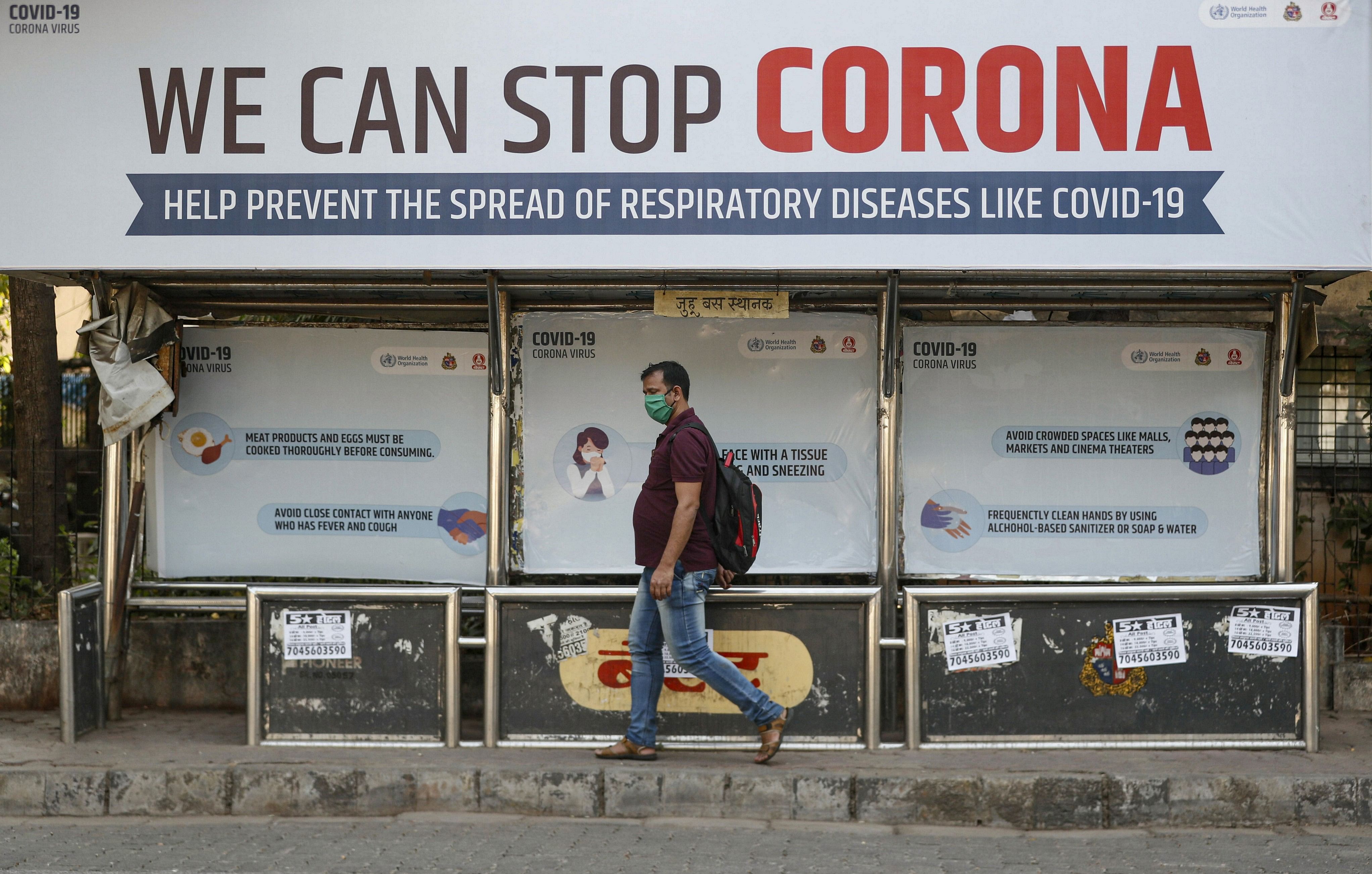 A man wearing a protective mask walks past a bus stop displaying preventive measures against the coronavirus in Mumbai. (Credit: Reuters)