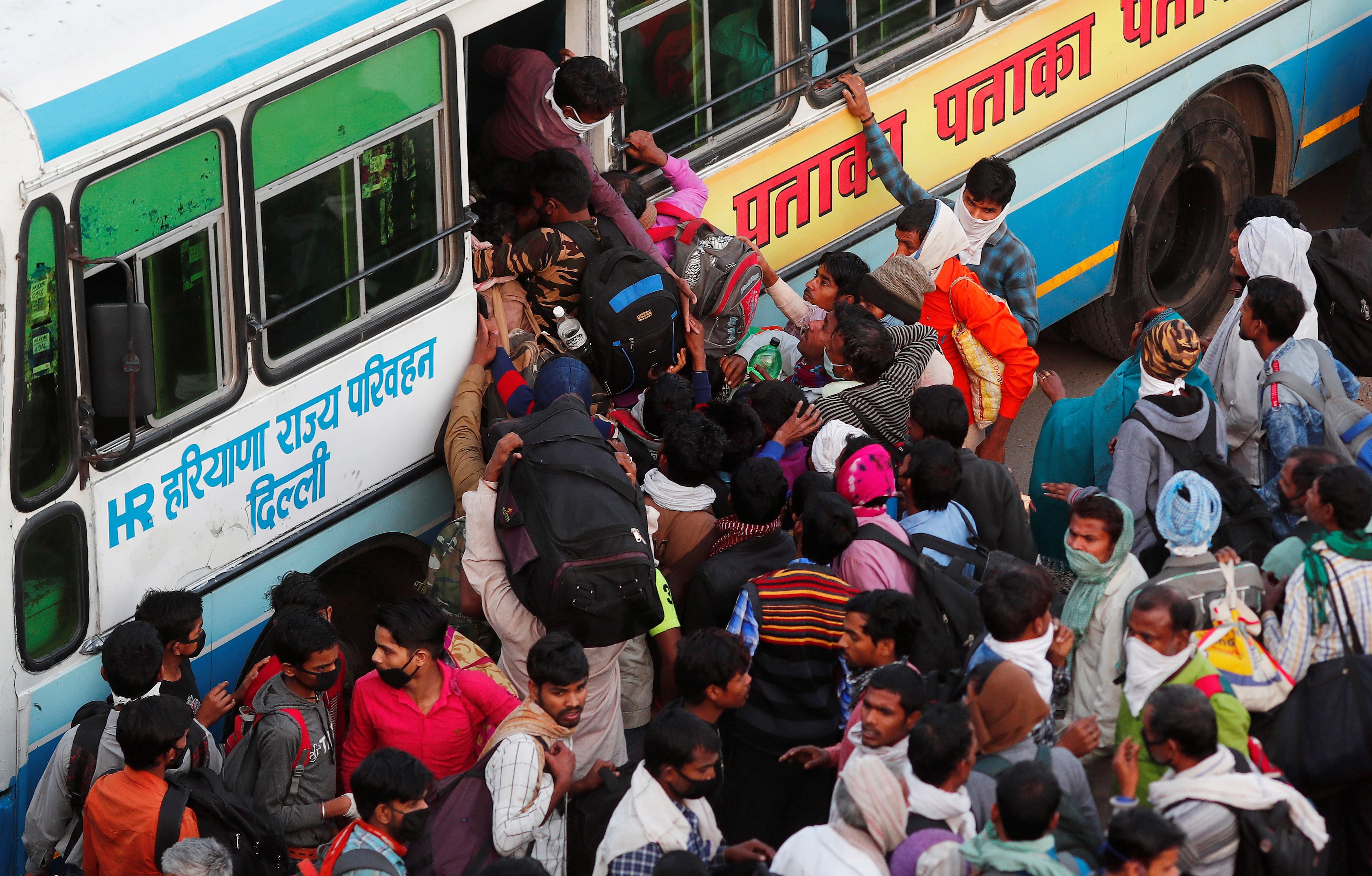 Migrant workers try to board a crowded bus as they return to their villages, during a 21-day nationwide lockdown to limit the spreading of coronavirus disease (COVID-19), in Ghaziabad, on the outskirts of New Delhi. (Credit: Reuters)