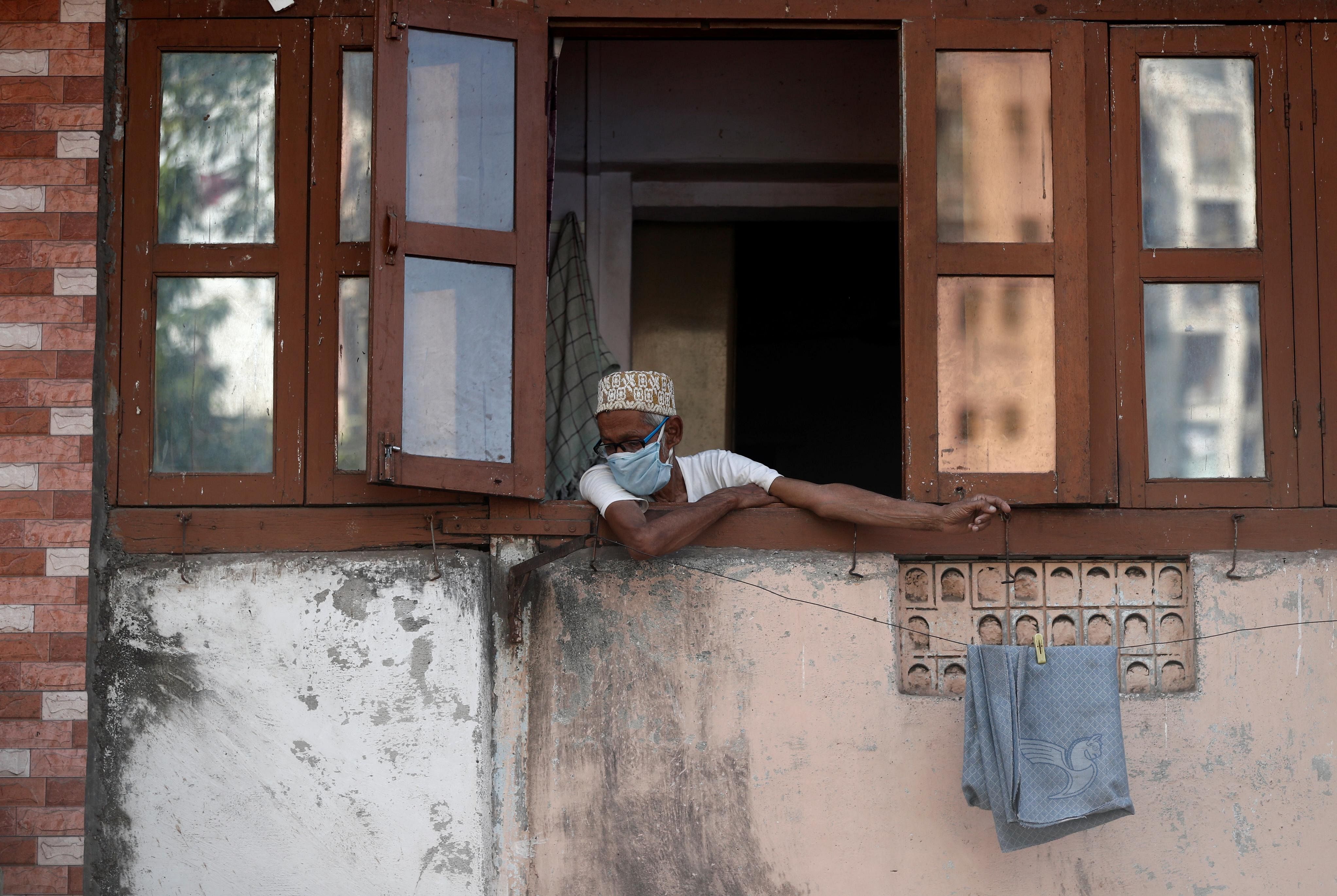 A man wearing a protective face mask looks out of the window during a 21-day nationwide lockdown in Mumbai. (Credit: Reuters)