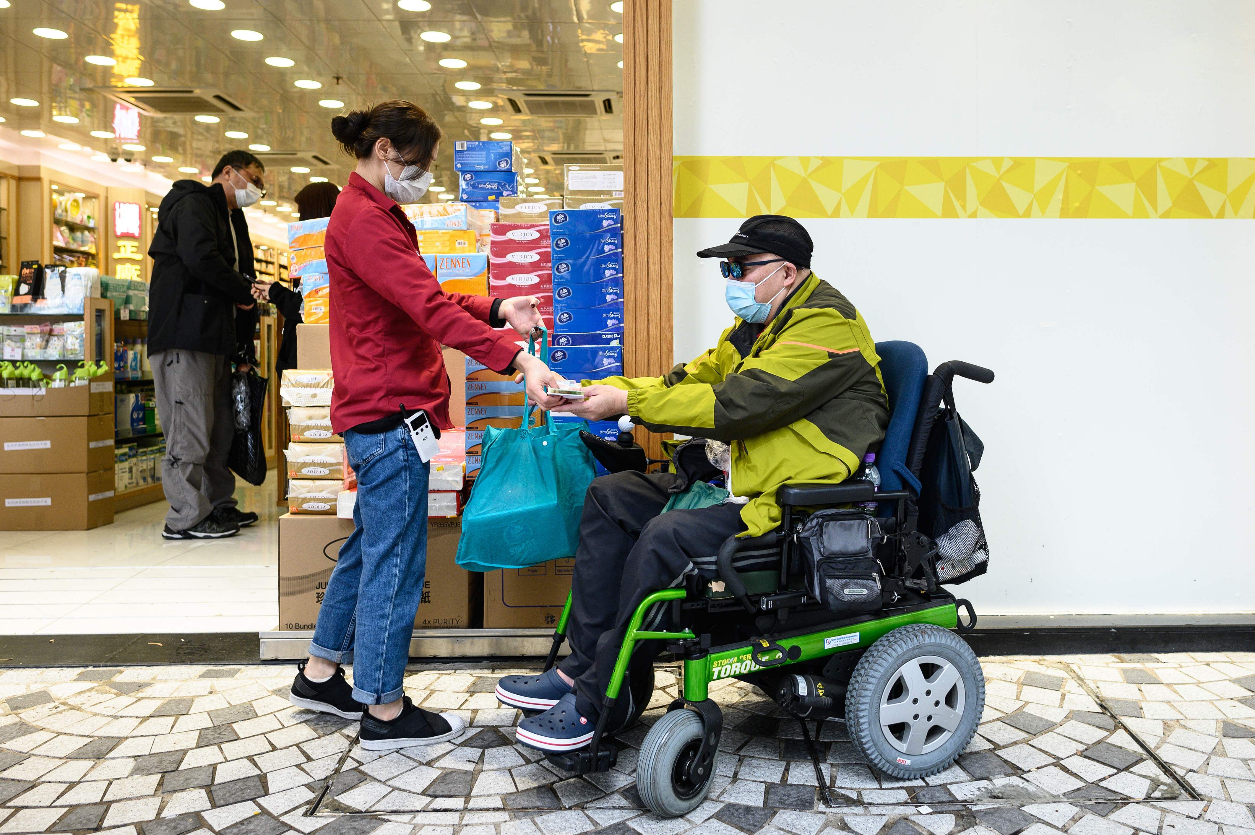 This photo taken on February 13, 2020 shows muscular atrophy patient Steven Yan (R) buying a bag of paper towels from a pharmacy in the Sheung Shui district of Hong Kong. (Credit: AFP Photo)