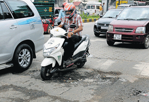 Poor condition: A motorist rides over a pothole on Bannerghatta Road.