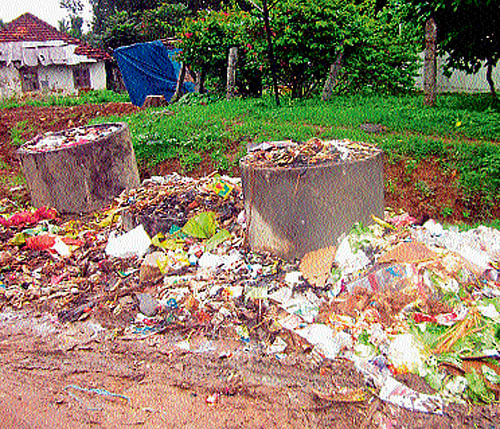 Students are forced to walk on the muddy road at Thithimathi near Gonikoppa. (Below) Overflowing dustbins have been posing threat to the lives of the residents. dh photos