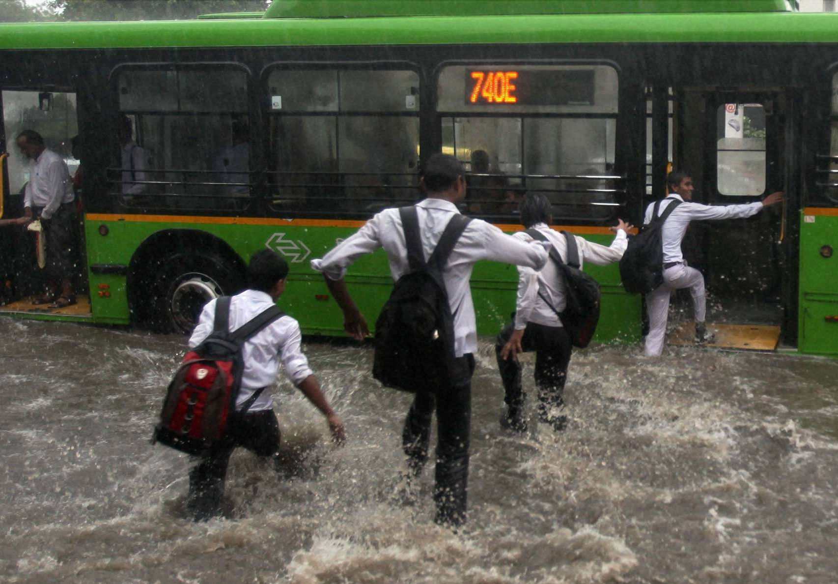Students run through rain water to board a bus during heavy shower in New Delhi on Saturday. PTI Photo