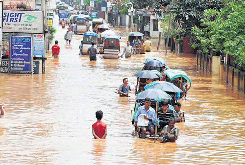 Rickshaw-pullers and people wade through a water-logged street after heavy rain in Guwahati on  Friday. PTI photo