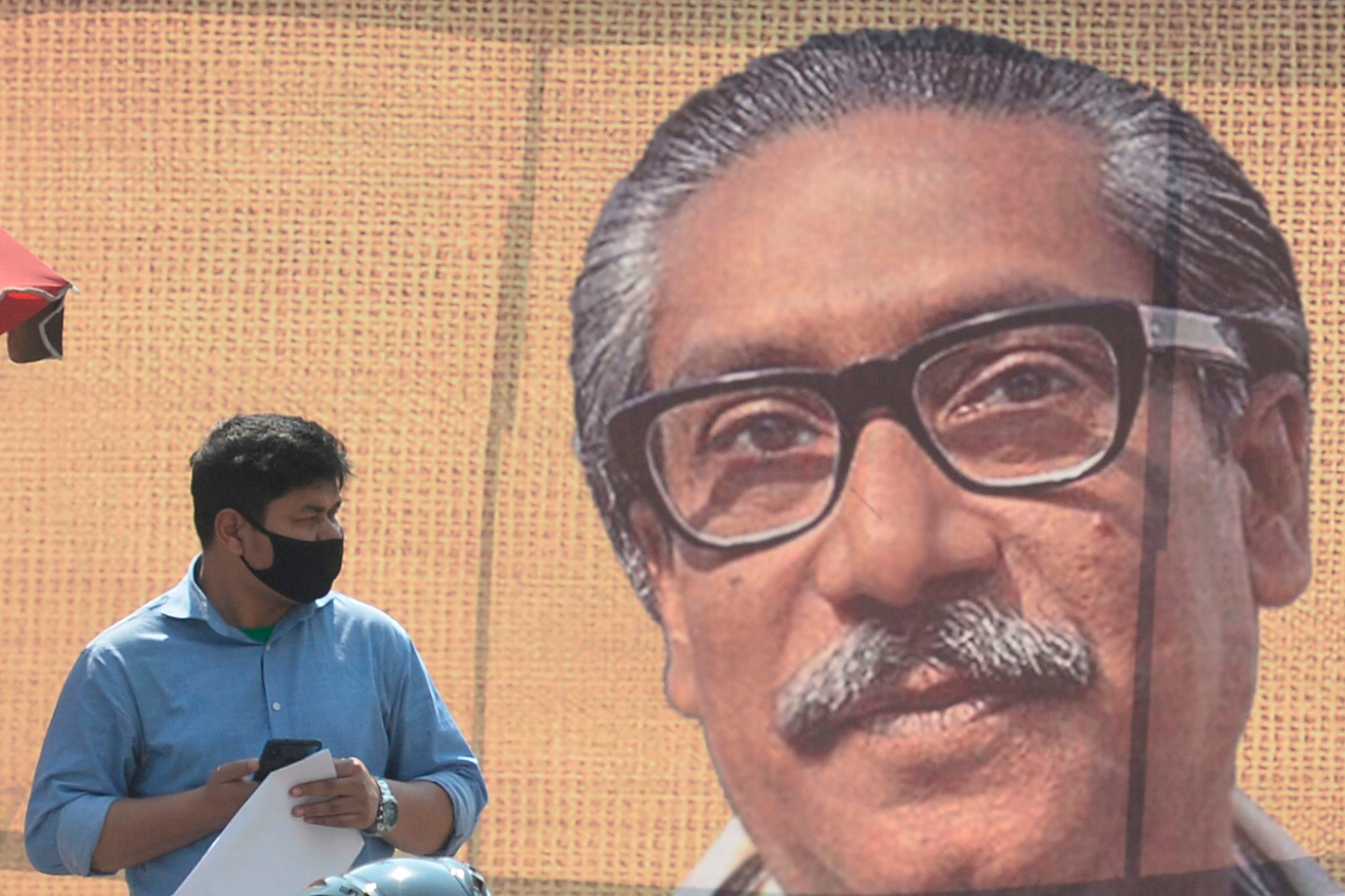 A man wearing a facemask amid fears of the spread of COVID-19 novel coronavirus, walks past a banner with a picture of Bangladesh’s founder Sheikh Mujibur Rahman. (AFP Photo)