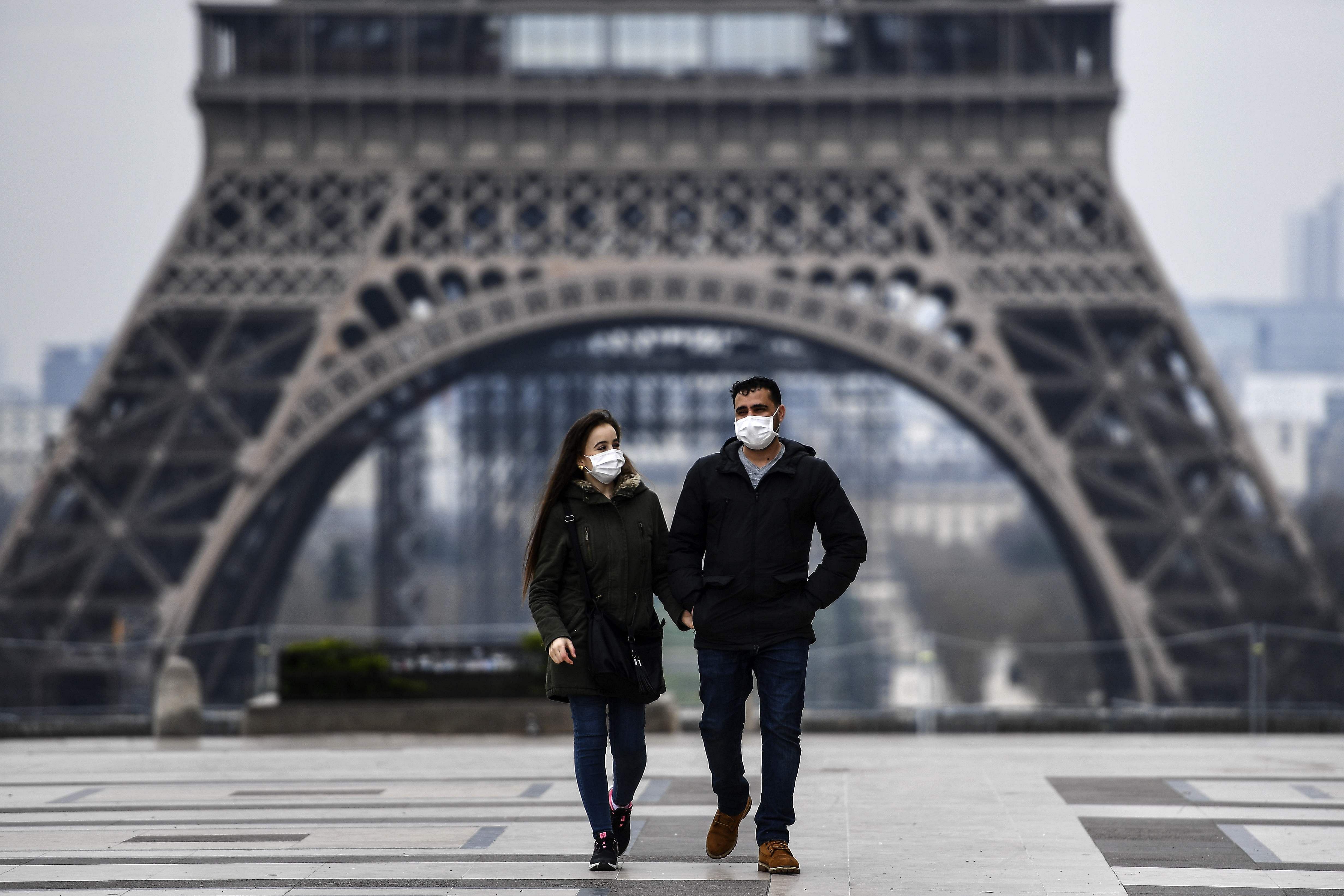 A couple wearing protective mask walks by the Esplanade du Trocadero square near the Eiffel Tower in Paris (AFP photo)