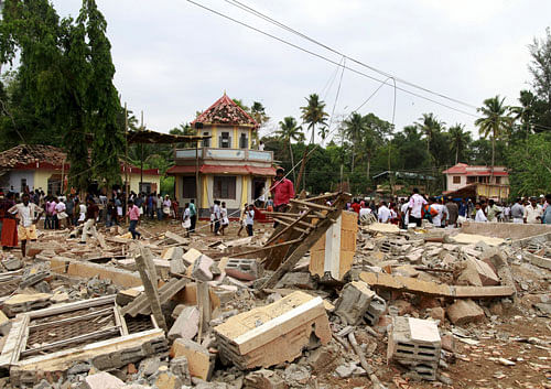 People stand next to debris after a cracker explosion at a temple in Kollam, on Sunday. REUTERS
