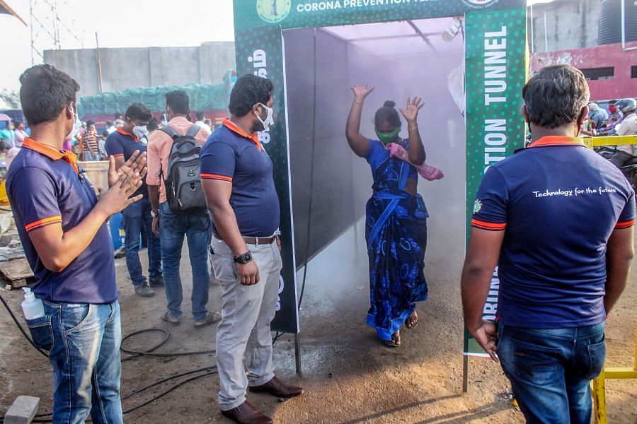 A woman walks through a disinfection tunnel set up at the entrance of Thennampalayam market in Tiruppur. Credit: AFP Photo