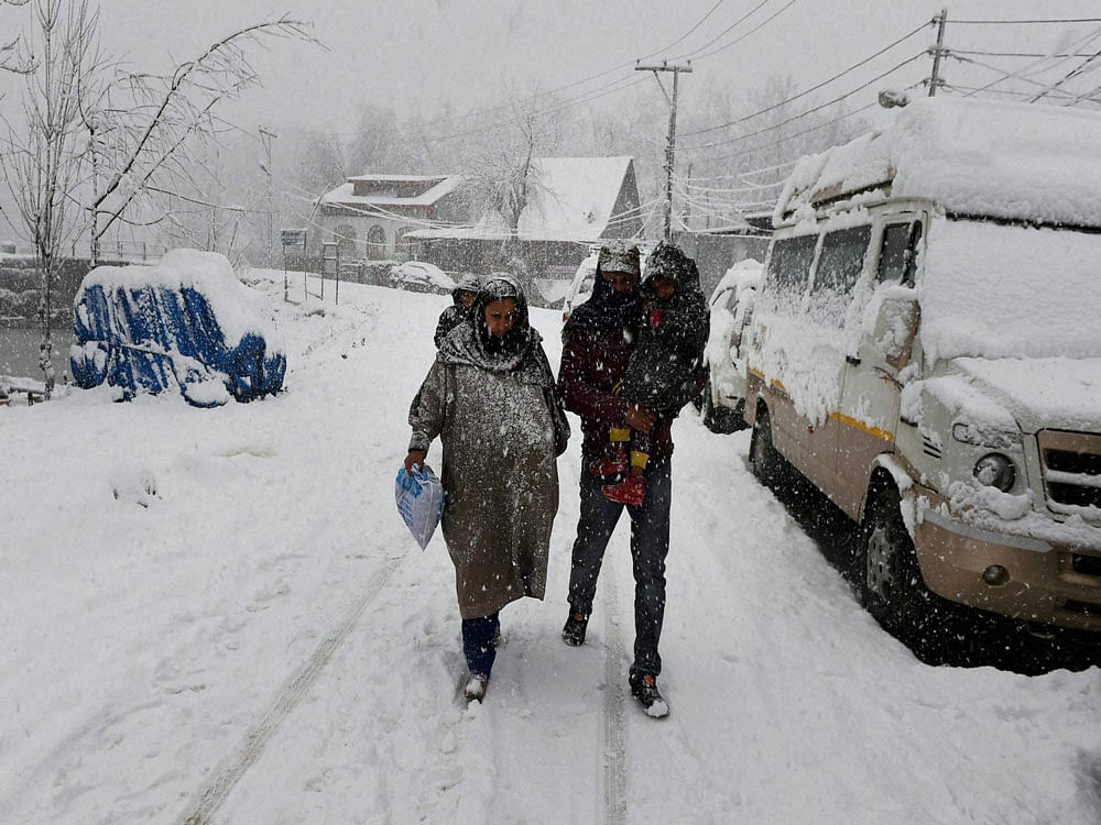 A couple with their child walks during heavy snowfall in Srinagar on Friday. Kashmir valley was cut off from rest of the country due to cancellation of flights and closure of Srinagar-Jammu national highway after heavy snowfall of the the season. PTI Photo
