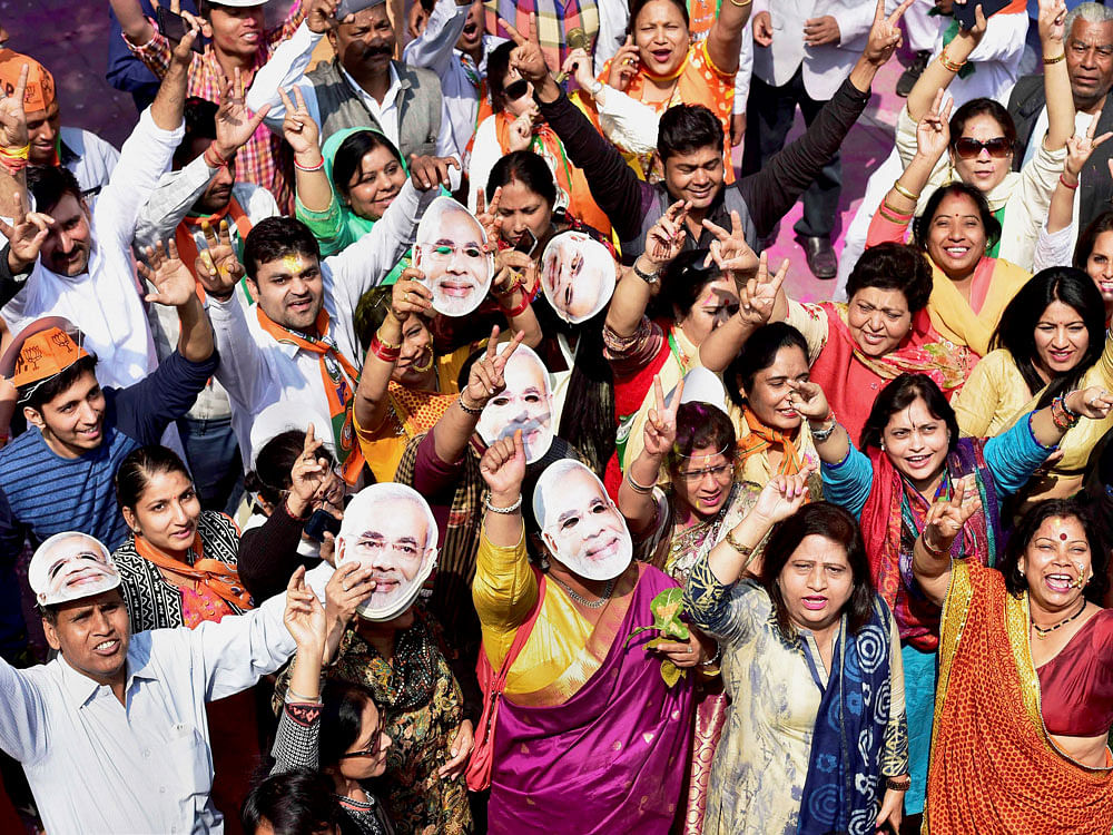 BJP workers and supporters, wearing the mask of Prime Minister Narendra Modi, celebrate the party's victory in the assembly elections, at party headquarters in New Delhi on Saturday. PTI Photo