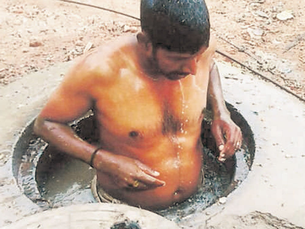 Civic worker Ganesh gets into a manhole to clean it near Chamundi Hill in  Mysuru on Tuesday. DH photo