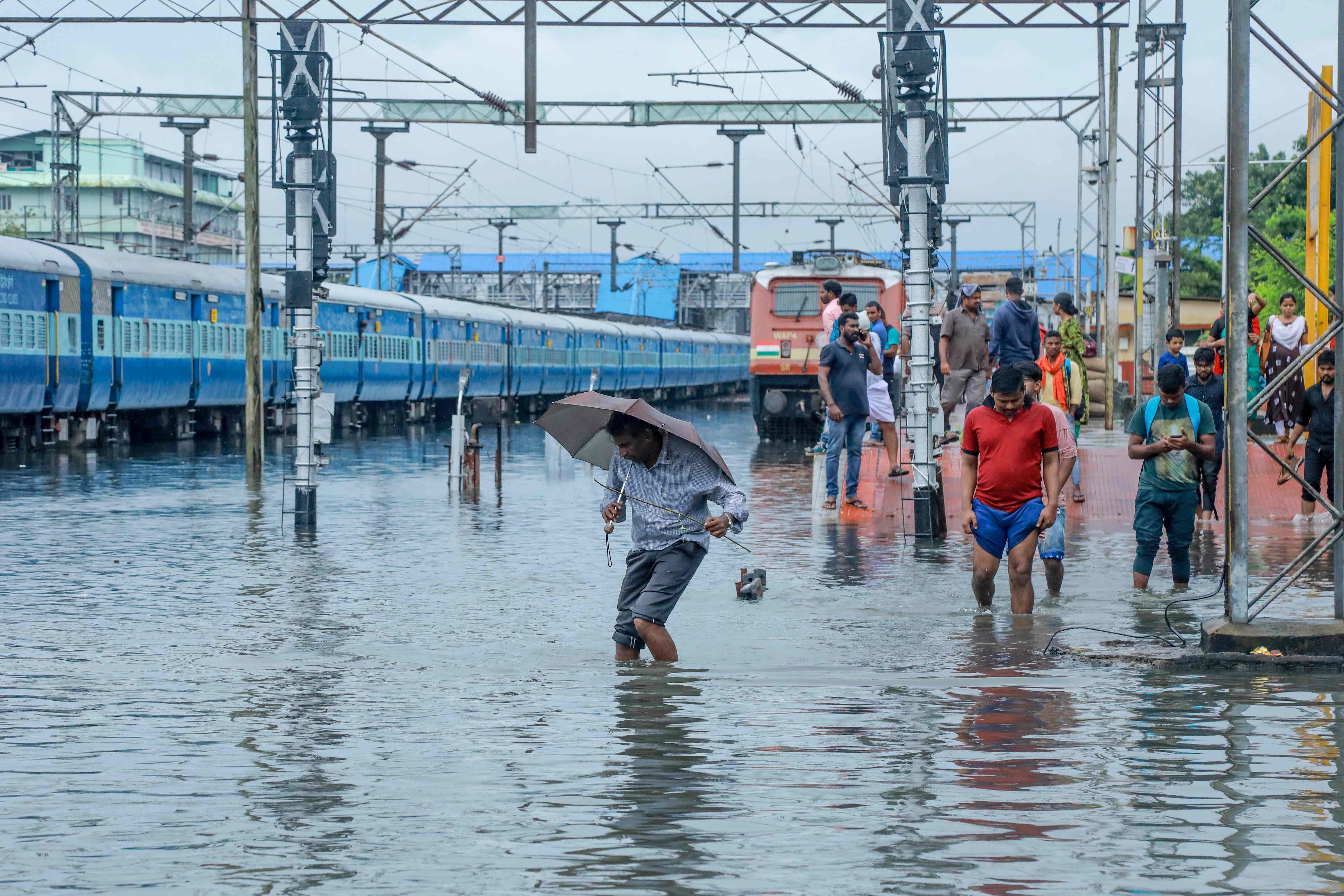 Passengers walk on waterlogged rail tracks at Ernakulam Junction station in Kochi in the southwestern Indian state of Kerala. (PTI Photo)