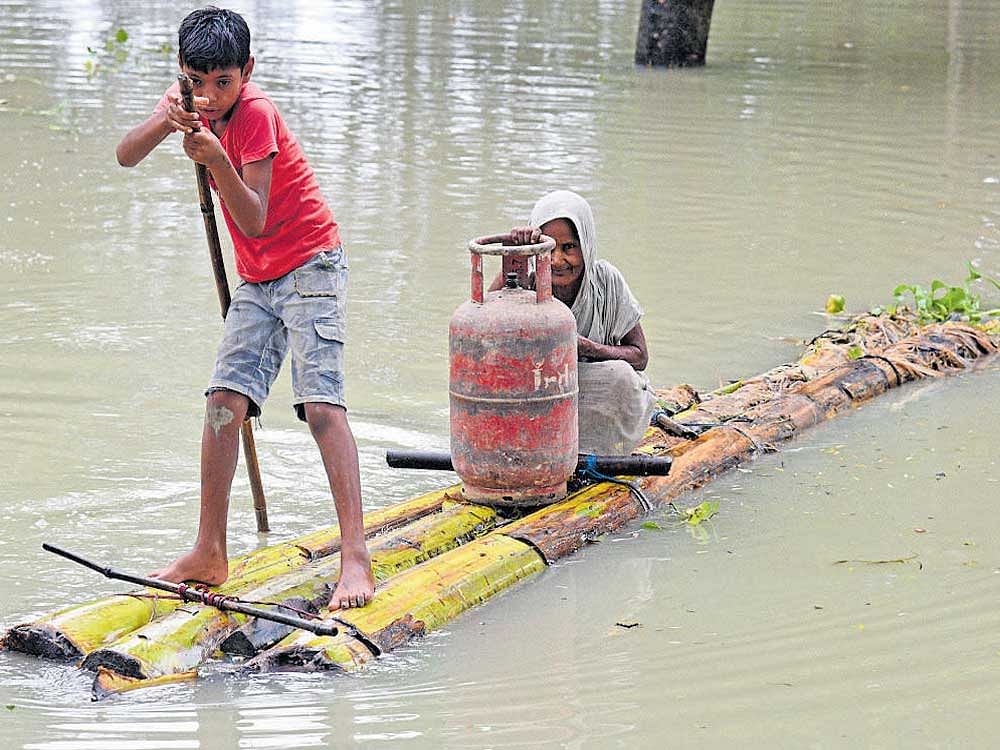A boy rows a makeshift raft as he transports a woman and a cooking gas cylinder through flood waters in Morigaon district of Assam