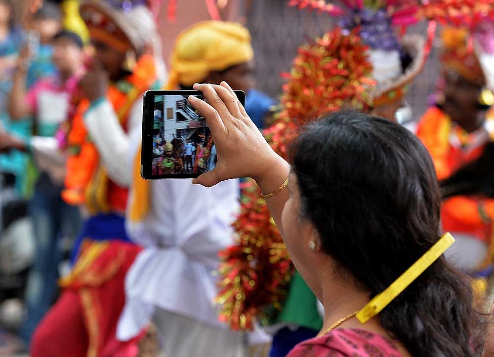 A woman taking pictures in her mobile of a colourful procession on the street, in Bengaluru. DH File Photo by ANAND BAKSHI