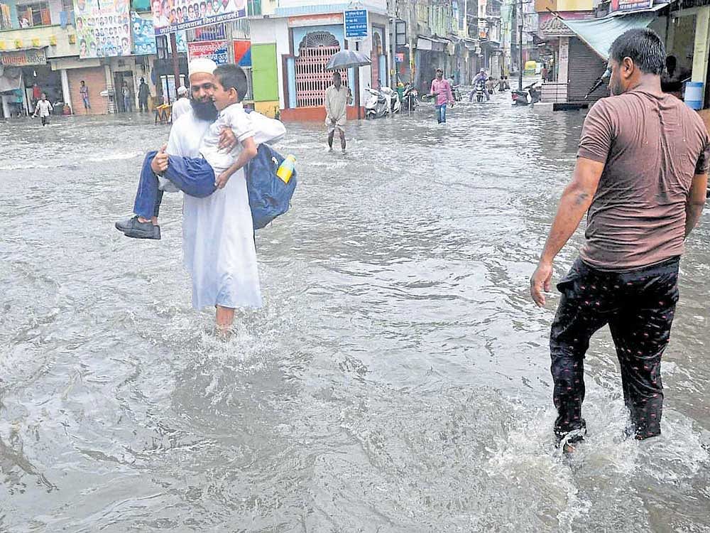 Commuters wade through waterlogged street after heavy rain in Ujjain, Madhya Pradesh on Monday. PTI