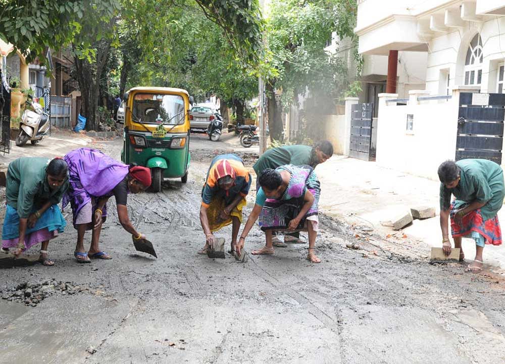 Workers cleaning silt and sewage from a road in Koramangala on Saturday. DH Photo