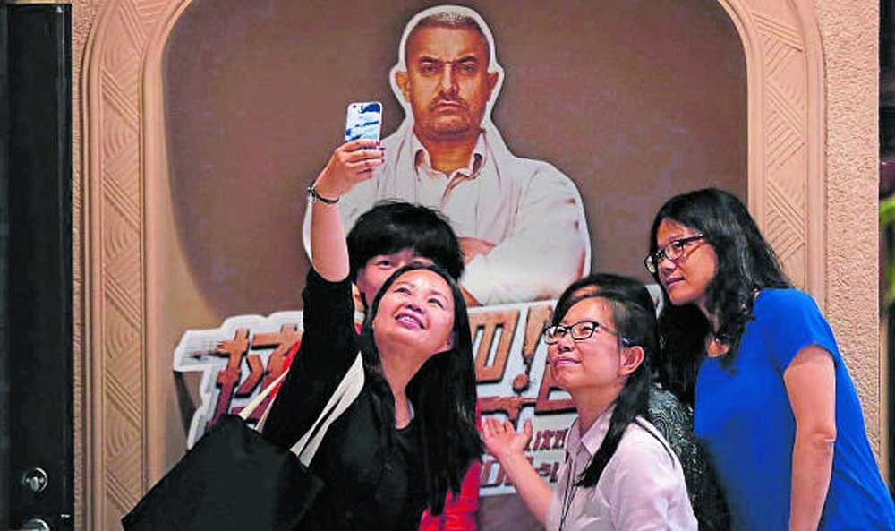 in thrall: Chinese women pose in front of a Dangal poster at a Beijing theatre. The movie's runaway success has prompted Chinese production companies to snap up all things Bollywood - partnerships and distribution rights, but also Indian directors and screenwriters. AP