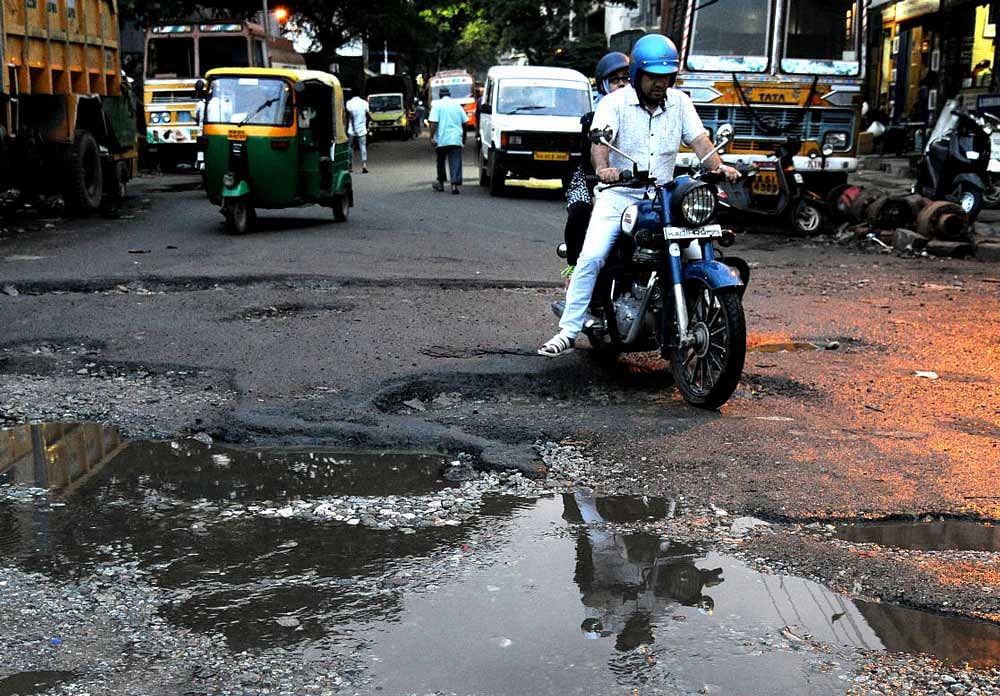 A two-wheeler rider struggles to negotiate the pothole-ridden Siddaiah Road on Saturday. Dh Photo/Srikanta Sharma R.