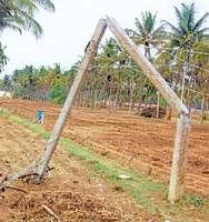 The electric pole which broke off owing to the gusting winds on Tuesday in a field near Petechamanahalli. The pole was not  removed even on Thursday. DH Photo