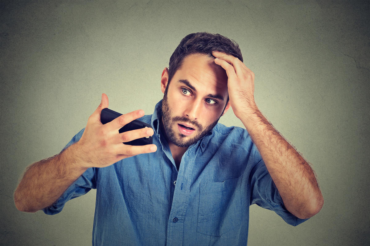 Closeup portrait, shocked man feeling head, surprised he is losing hair, receding hairline, bad news isolated on gray wall background. Negative facial expressions, emotion feelingBaldness
