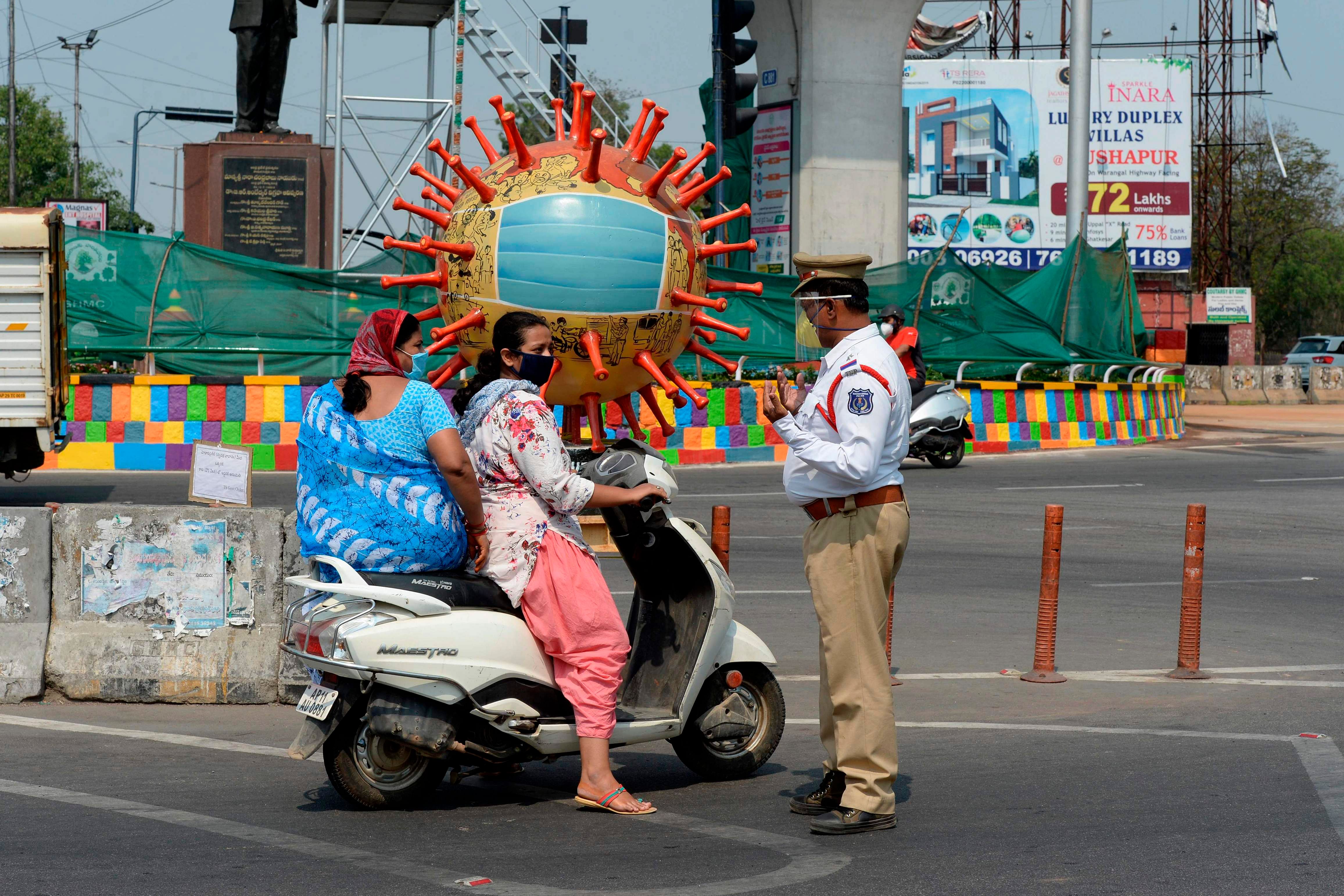 A traffic police officer (R) stands infront of a coronavirus-themed globe at a traffic junction enquire people travel during a government-imposed nationwide lockdown. (AFP Photo)