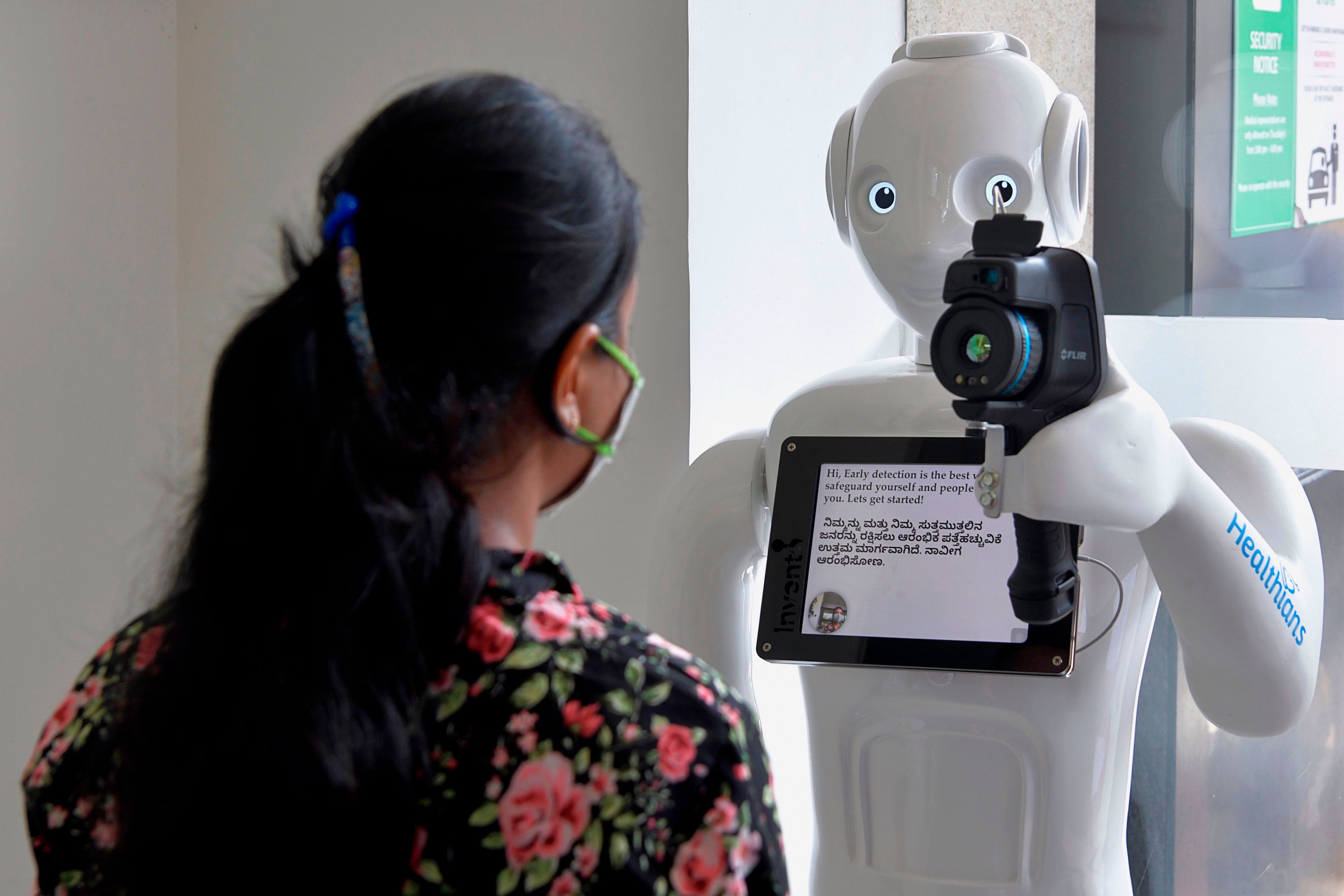 A patient gets her temperature checked by 'Mitra', a robot equipped with a thermal camera installed to register and conduct preliminary screening of patients before directing them to respective medical specialists, (Credit: AFP)