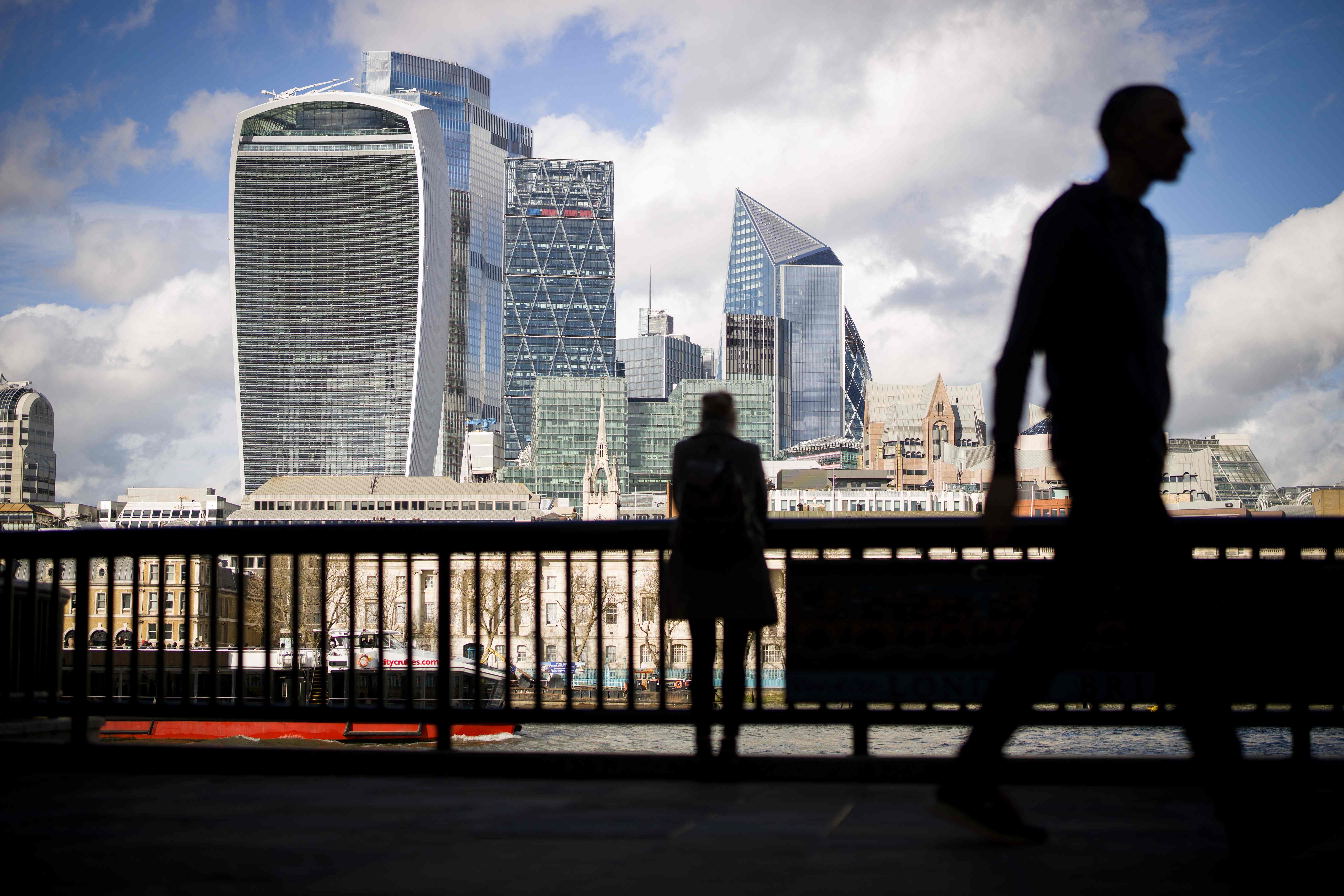 Pedestrians walk by with the towers of the City of London in the background in London. (AFP photo)