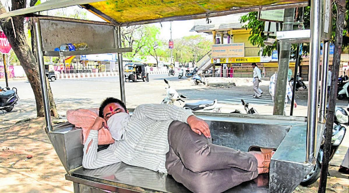A man takes shelter in a food stall as temperatures soared above normal in Kalaburagi on Wednesday. (DH photo)