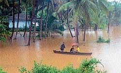 Residents using a boat to reach their home in Adamkudru in Mangalore on Friday. DH Photo