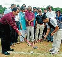 Former international hockey player Mohan K T plays hockey with Central excise Superintendent, Ashoka D to inaugurate the district-level hockey tournamant in Mysore on Monday. Journalist Rajashekar Koti is seen. DH photo
