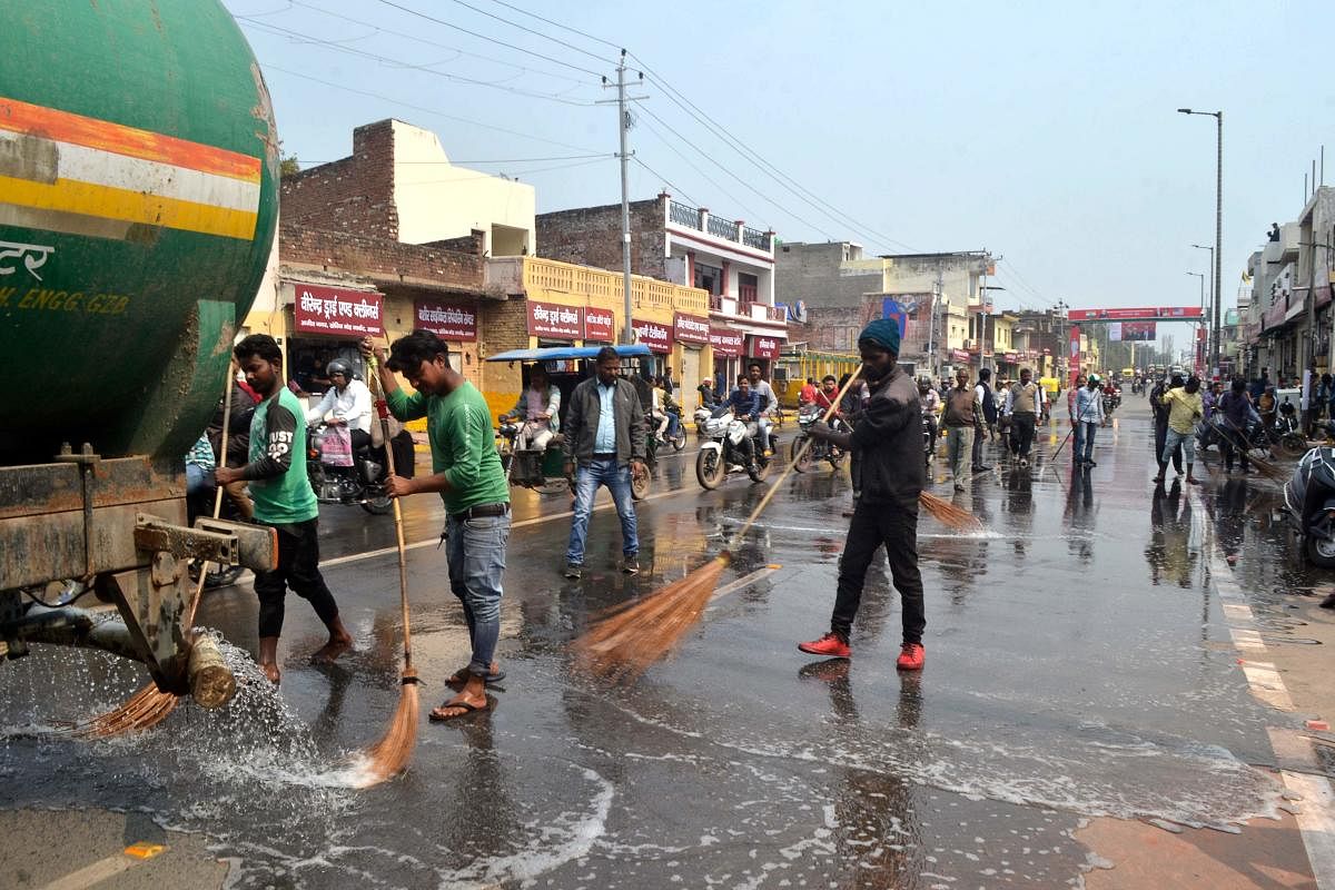 Workers wash a road with water near Kheria Airport in Agra. (AFP Photo)